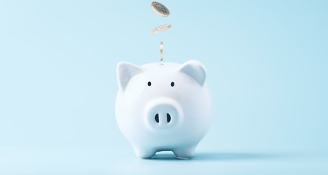 White piggy bank with coins dropping in, representing savings and cost efficiency.